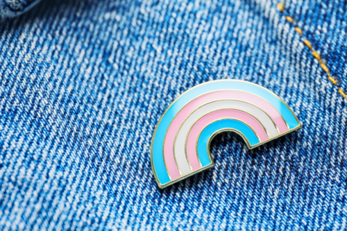 Enamel trans pin badge on a light denim jacket.