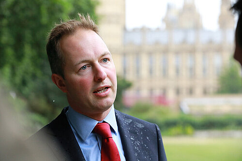 Richard Foord speaking to someone with the Houses of Parliament in the background