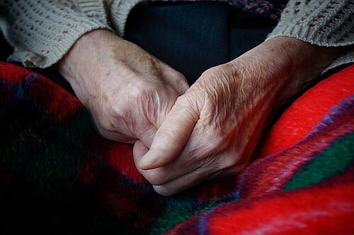 An elderly person's hands clasped together over a blanket