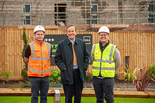 Three men - two in hi vis - one (Martin Tod) in a suit and coat - standing in front of a construction site with a Cala sign