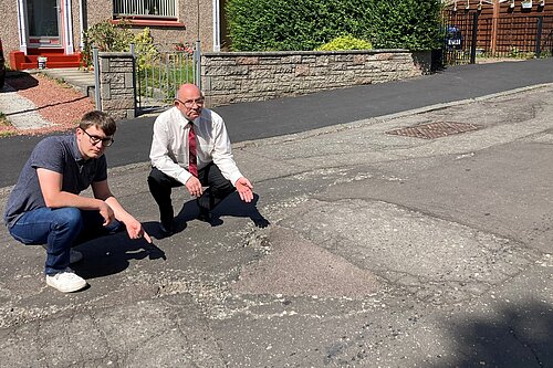 Cllrs Aldridge and Thornley pointing at a pothole on Clermiston Crescent
