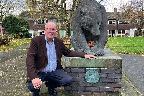 Cllr Fenton kneeling by the Chalfonts Bear plinth, with its newly reinstated plaque
