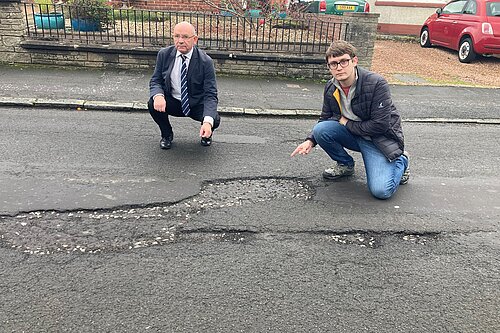 Cllrs Thornley and Aldridge pointing at a pothole on Parkgrove Drive