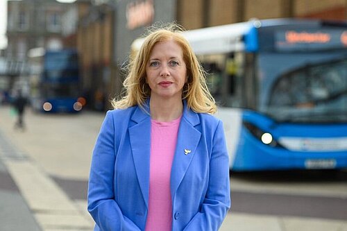 Liz Jarvis, MP for Eastleigh, stands in a blue jacket in front of a bus.