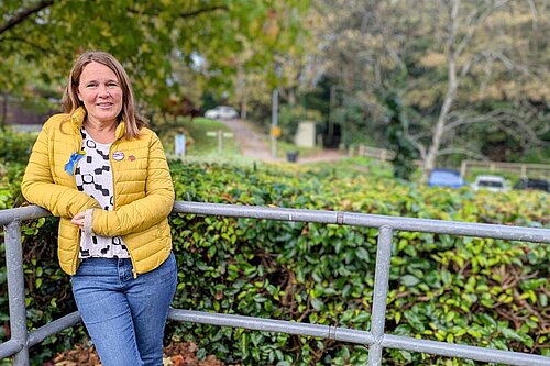 Vikki stood in front of a hedge leaning on a railing