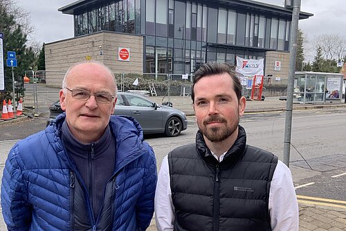 Vaughan Moody and Adam Harley standing on the pavement with Bearsden Community Hub in the background surrounded by metal fencing.