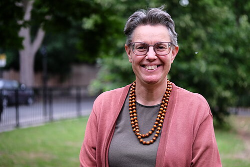 Photo of Janet Grauberg wearing a pink cardigan against a leafy green background