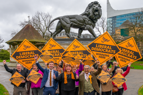 The Reading Liberal Democrats, cheering and holding orange diamond placards, in front of the Maiwand Lion