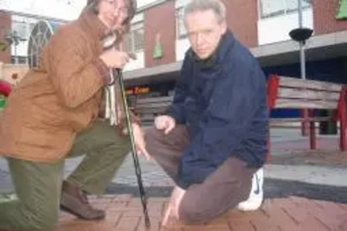 Cllr Ros Webb and Stephen Robinson crouching and pointing at loose paving stones at Market Square