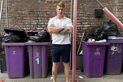 Cllr Carl Cashman standing in front of overflowing bins