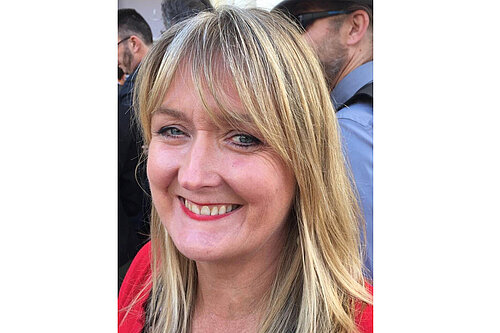 Stella Spiteri, a white woman with shoulder length blonde hair, smiles at the camera as if she has just won something..